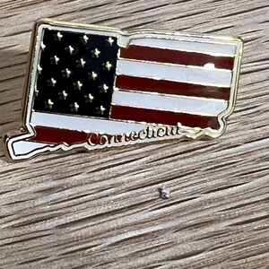 May include: Gold-colored pin shaped like the state of Connecticut with an American flag design and the word "Connecticut" written below the flag.
