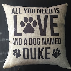 May include: A gray throw pillow with black text that reads "All you need is LOVE and a dog named DUKE". The text is surrounded by paw prints.