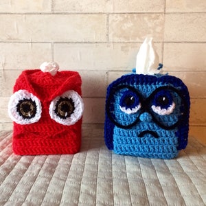 May include: Two crocheted tissue box covers, one red with angry eyes and one blue with sad eyes and glasses.