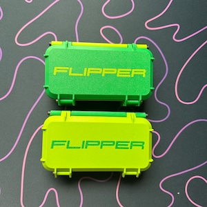May include: Two green and yellow plastic cases with the word "FLIPPER" printed on them.