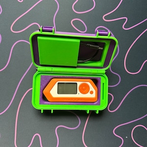 May include: A purple and green carrying case with a small orange device inside. The device has a screen and buttons and says "SMARTSTEP" on it.
