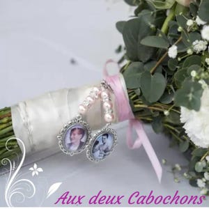May include: A bridal bouquet featuring pink roses, white carnations, and greenery. The bouquet is adorned with two silver photo charms and tied with a satin ribbon. The text "Aux deux Cabochons" is visible at the bottom.