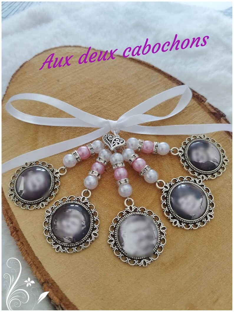 May include: A handmade photo charm with six circular pendants featuring a grayscale image, each framed in ornate silver filigree. The charms are connected by pink and white beads, a silver heart, and a white ribbon. The text "Aux deux cabochons" is visible.
