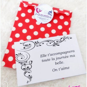 May include: A red polka dot gift bag with a white card. The card has black decorative flourishes and the text "Elle t'accompagnera toute la journ&eacute;e ma belle. On t'aime. Aux deux cabochons."