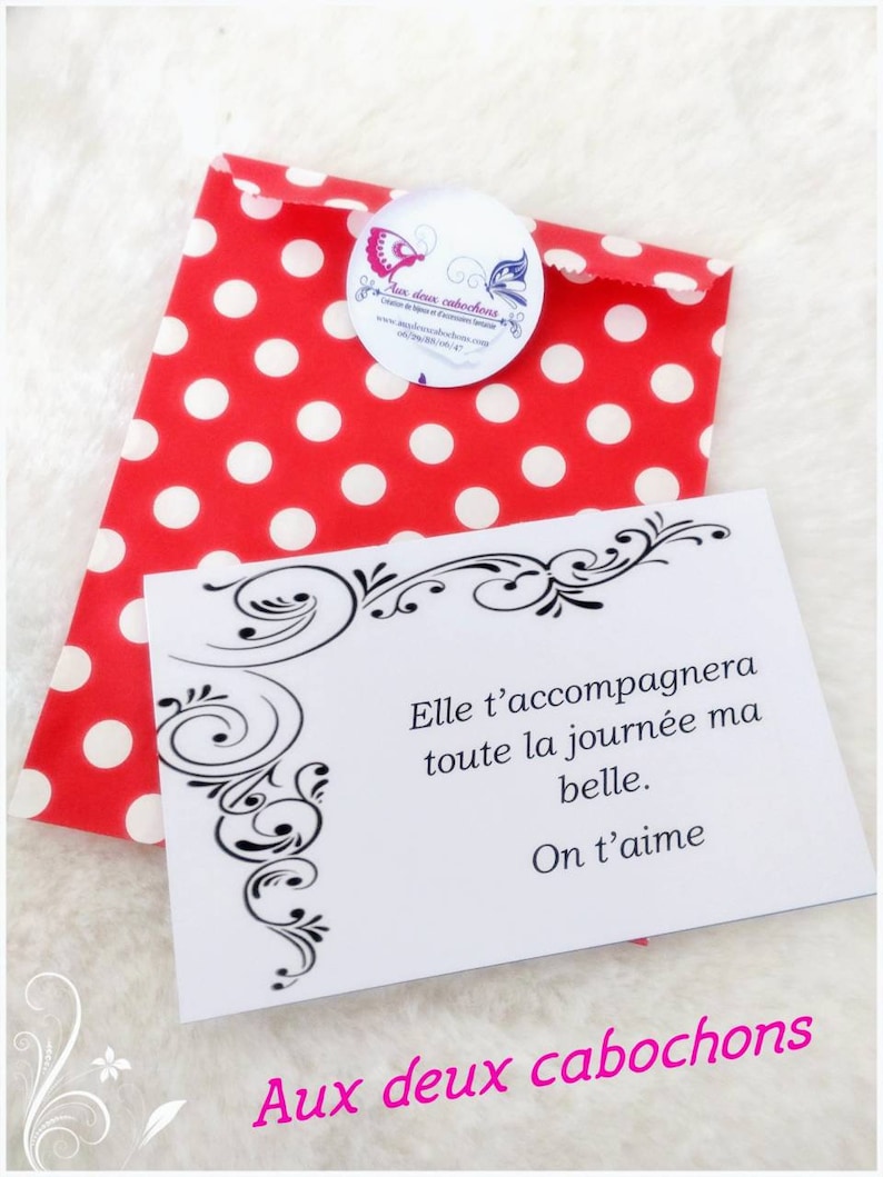 May include: A red polka dot gift bag with a white card. The card has black decorative flourishes and the text "Elle t'accompagnera toute la journ&eacute;e ma belle. On t'aime. Aux deux cabochons."