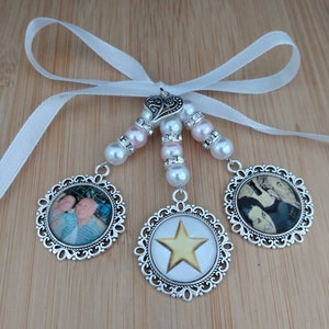 May include: A decorative charm with three round pendants, each with a different design. The pendants are connected by beaded strands of pearls and pink beads, and a white ribbon. The pendants feature photos and a gold star.