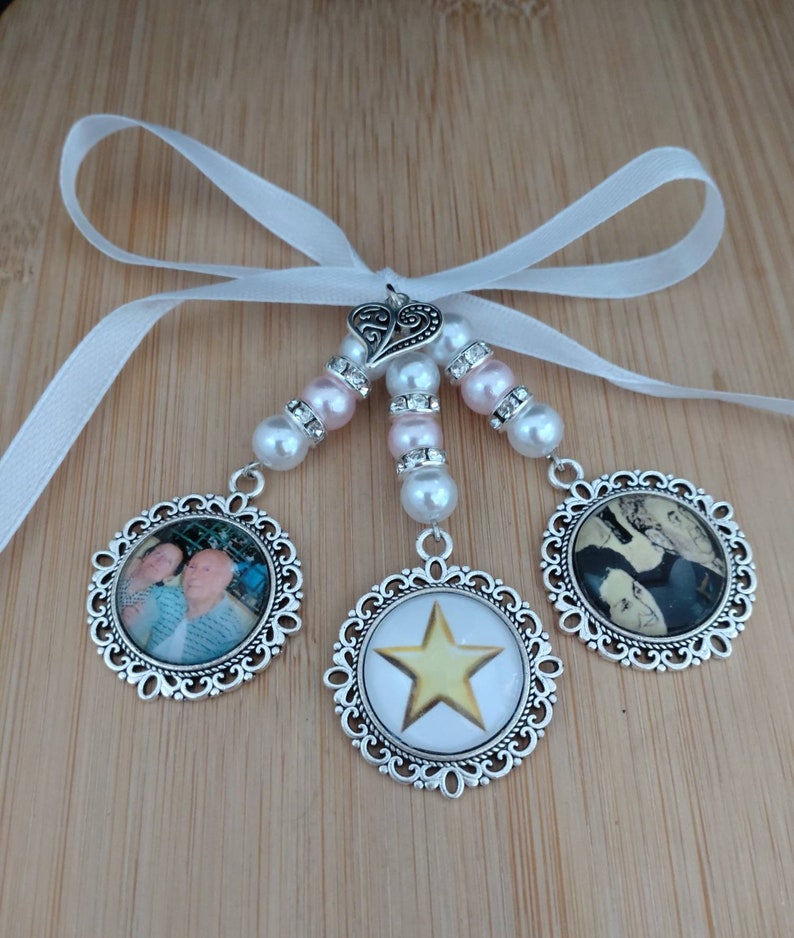 May include: A decorative charm with three round pendants, each with a different design. The pendants are connected by beaded strands of pearls and pink beads, and a white ribbon. The pendants feature photos and a gold star.
