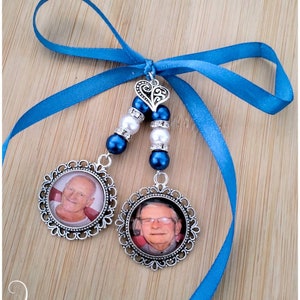 May include: A memorial keepsake featuring two photo pendants with silver filigree frames, suspended from a blue ribbon. Each pendant displays a portrait. The ribbon is tied with a decorative heart charm and beaded accents.
