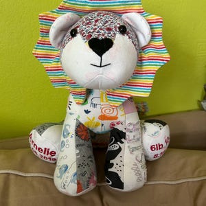 May include: A handmade lion plush toy with a rainbow mane and floral patterned head. The lion's body is made of various patterned fabrics. The lion's paw reads "Amelie 2019" and "6lb 10 8.1".