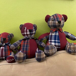 May include: Three plaid teddy bears, one large, one medium, and one small, sitting on a couch. The bears are made from different types of plaid fabric and have embroidered details, including the names "Grandad" and "Ella" and the date "16.7.2021".