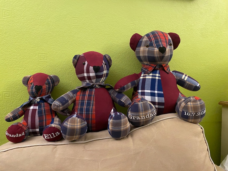 May include: Three plaid teddy bears, one large, one medium, and one small, sitting on a couch. The bears are made from different types of plaid fabric and have embroidered details, including the names "Grandad" and "Ella" and the date "16.7.2021".