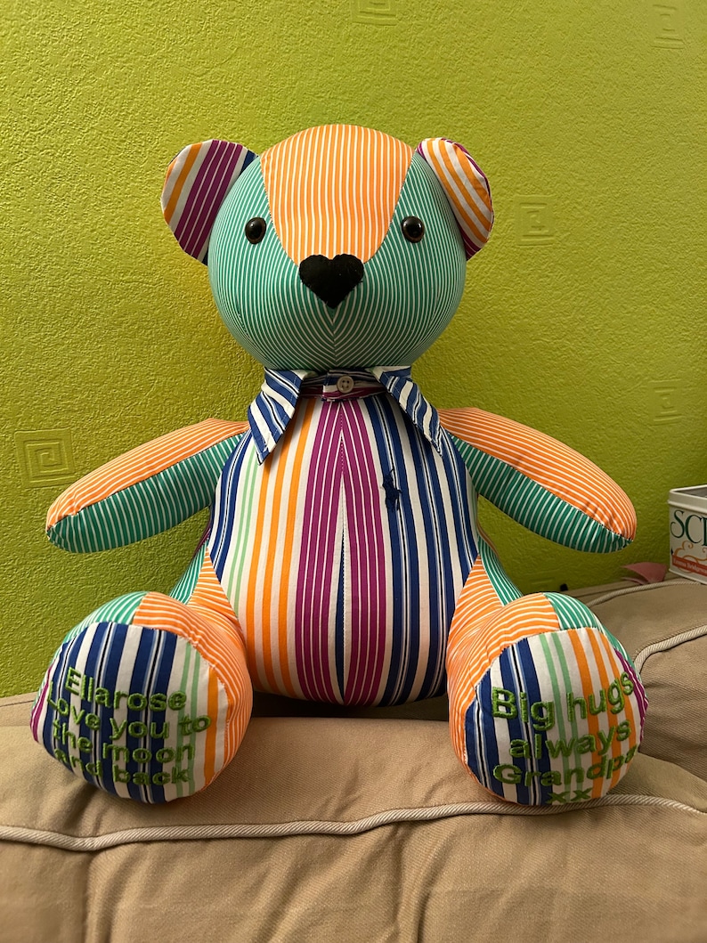 May include: A colorful striped teddy bear wearing a shirt with a bow tie. The bear has embroidered text on its paws that reads "Ella rose love you to the moon and back" and "Big hugs always Grandpa".