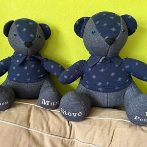 May include: Two blue teddy bears with embroidered names on their feet. The bears are wearing blue shirts with a white pattern. The bears are sitting on a light brown surface.