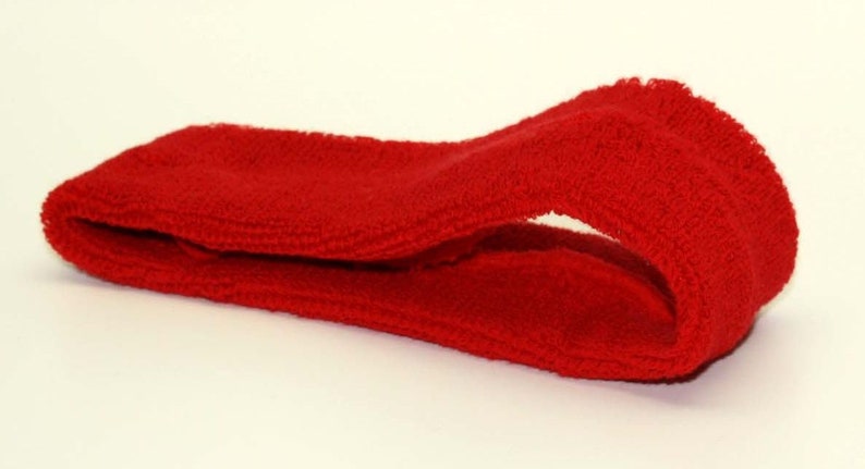 Peut inclure: Un bandeau rouge en tissu doux et extensible. Il est pli&eacute; en deux et pos&eacute; sur une surface blanche.