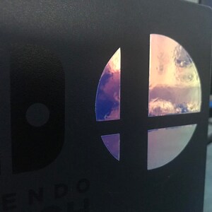 May include: A black Nintendo Switch game case with a holographic Super Smash Bros. logo.