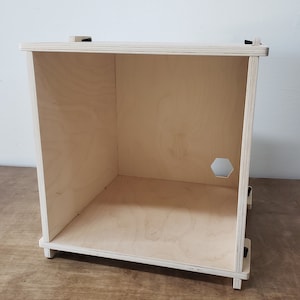 May include: A plain wooden box with a hexagonal hole cut out of one side. The box is made of plywood and has a light wood finish.