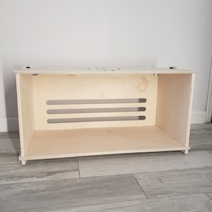 May include: A light wood storage shelf with three horizontal slots and a small, hand-shaped cutout on the front.