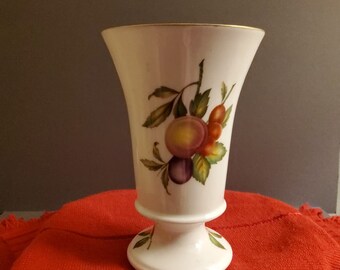 May include: A white ceramic vase with a gold rim and a floral design featuring plums, peaches, and berries.