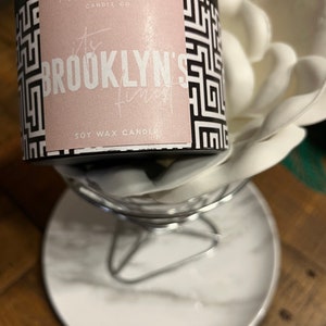 May include: A black and white geometric patterned candle jar with a pink label that reads "The Brooklyn's Finest Soy Wax Candle".