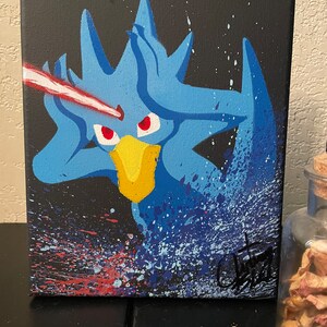 May include: A blue and yellow cartoon character with red eyes is painted on a black canvas. The character is surrounded by blue, white, and red paint splatters. The canvas is signed in the bottom right corner.