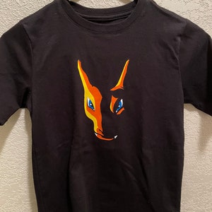 May include: Black t-shirt with a graphic of a cartoon orange and yellow creature with blue eyes.