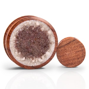 Puede incluir: Un par de dilatadores de oreja de madera con incrustaciones de cristal. El dilatador más grande tiene un exterior de madera marrón con una incrustación de cristal transparente que tiene un tono púrpura. El dilatador más pequeño está hecho de madera marrón.