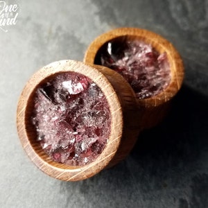 May include: Pair of wooden ear gauges with a red and clear crystal inlay. The gauges are round and have a wood grain pattern.
