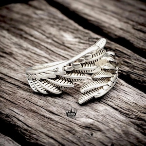 May include: A silver ring featuring a detailed design of two wings. The wings are crafted from small, intricate feathers.