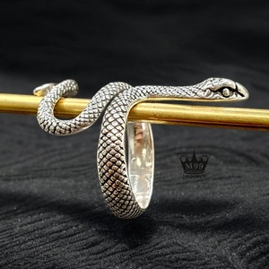 May include: A silver snake ring with a textured finish. The snake is coiled around the ring band and has a detailed head with eyes.