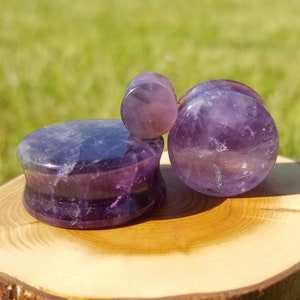 May include: Three amethyst stone ear gauges of different sizes. The gauges are purple and have a natural, polished finish.