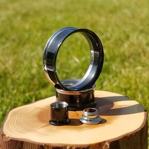 Peut inclure: Un ensemble de trois jauges d'oreille noires et argentées. Les jauges sont en métal et ont une finition lisse et polie. La plus grande jauge est un anneau avec un bord extérieur noir et un bord intérieur argenté. Les deux autres jauges sont des bouchons avec un bord extérieur noir et un bord intérieur argenté.