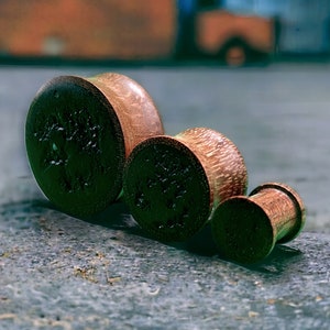 May include: Three wooden ear gauges of different sizes. The gauges are brown and have a wood grain pattern.