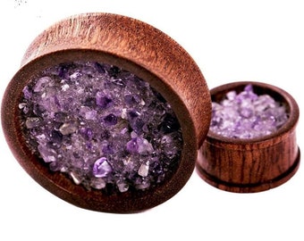 May include: A pair of wooden ear gauges with a purple amethyst stone inlay. The gauges are made of dark wood and have a smooth finish.