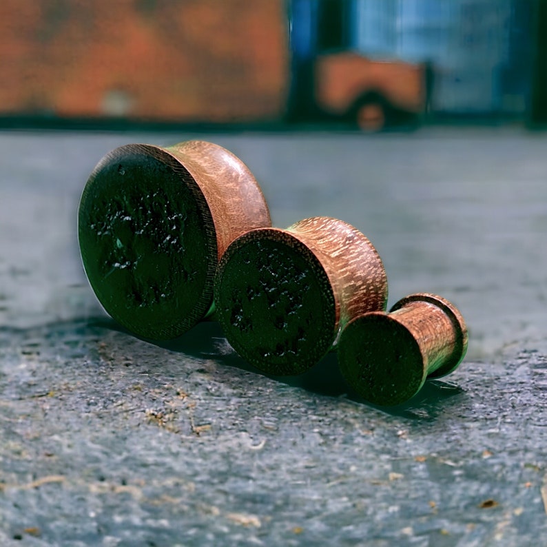 May include: Three wooden ear gauges of different sizes. The gauges are brown and have a wood grain pattern.