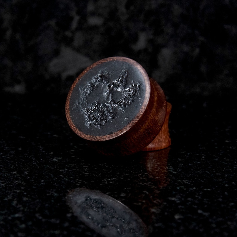 May include: A pair of wooden ear gauges with a black resin inlay featuring a unique design. The gauges are a dark brown color and have a smooth, polished finish.