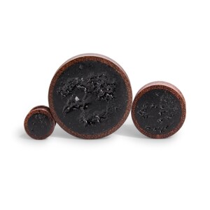 May include: Three wooden ear gauges with a black, speckled finish. The largest gauge is approximately 1.5 inches in diameter, the middle gauge is approximately 1 inch in diameter, and the smallest gauge is approximately 0.5 inches in diameter.