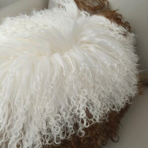 May include: A round, fluffy cushion with a white, curly fur exterior and a brown fur base. The cushion has a soft, inviting appearance, perfect for adding texture and warmth to any space. The fur appears to be natural and luxurious.