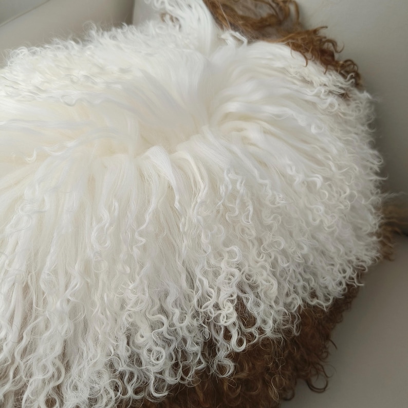 May include: A round, fluffy cushion with a white, curly fur exterior and a brown fur base. The cushion has a soft, inviting appearance, perfect for adding texture and warmth to any space. The fur appears to be natural and luxurious.