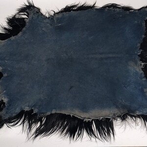 Puede incluir: Una alfombra de piel de oveja negra con un respaldo de cuero azul oscuro ligeramente desgastado. La piel es larga y gruesa, y los bordes est&aacute;n deshilachados.
