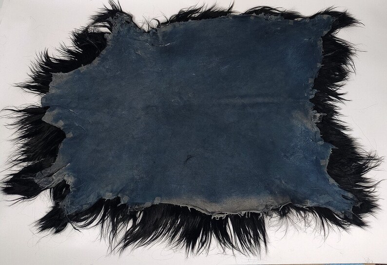 Puede incluir: Una alfombra de piel de oveja negra con un respaldo de cuero azul oscuro ligeramente desgastado. La piel es larga y gruesa, y los bordes est&aacute;n deshilachados.