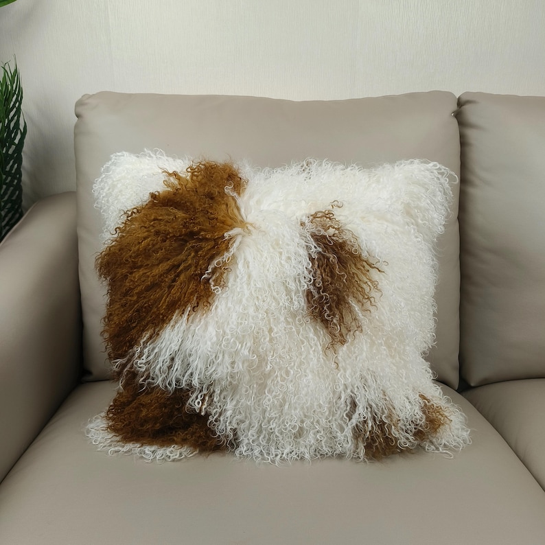 May include: A square decorative pillow with a shaggy, textured surface. The pillow features a pattern of white and brown fur, creating a unique and cozy aesthetic. The pillow is placed on a neutral-toned sofa.