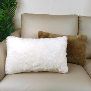 Peut inclure: Deux coussins moelleux sur un canapé brun clair. Le coussin de gauche est blanc et le coussin de droite est brun.