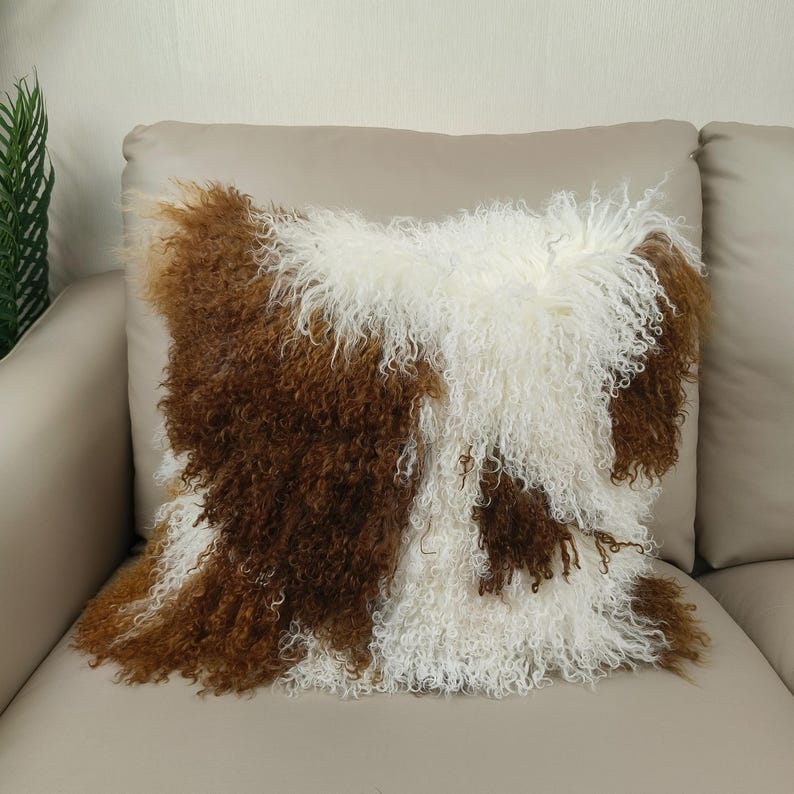 May include: A decorative throw pillow with a brown and white pattern. The pillow has a shaggy, textured appearance, with the brown sections resembling fur. The pillow is placed on a beige sofa, creating a cozy and inviting aesthetic.