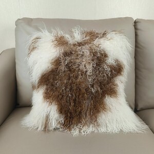 May include: Square decorative pillow with a brown and white fur design. The pillow has a soft, textured appearance, with the brown fur forming a central pattern against a white background. The pillow is placed on a neutral-toned sofa.