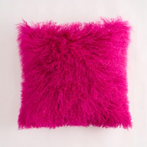 May include: A bright pink fluffy pillow made of sheepskin. The pillow is square and has a soft, plush texture.