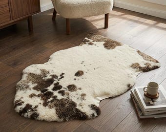 May include: A faux sheepskin rug featuring an irregular, organic shape with a cream-colored base and scattered dark brown patches. The rug has a thick, textured pile that mimics the appearance of animal fur, creating a soft and plush surface.