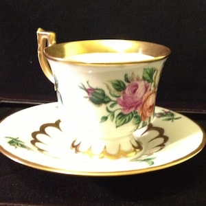 Könnte beinhalten: Eine weiße Teetasse und Untertasse mit goldfarbenem Rand und Blumenmuster. Die Tasse hat einen goldenen Henkel und die Untertasse einen gewellten Rand.