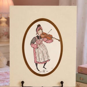 May include: A square print featuring an oval illustration of a person wearing a pink bonnet, a pink patterned dress, and a white apron, playing a brown violin. The print is set on a cream background and is displayed on a black metal stand.