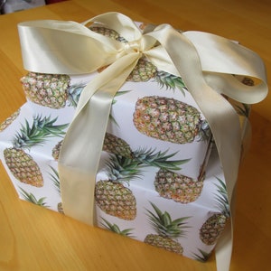 A stack of pineapple paper-wrapped gifts tied up with a luxurious cream silk ribbon.