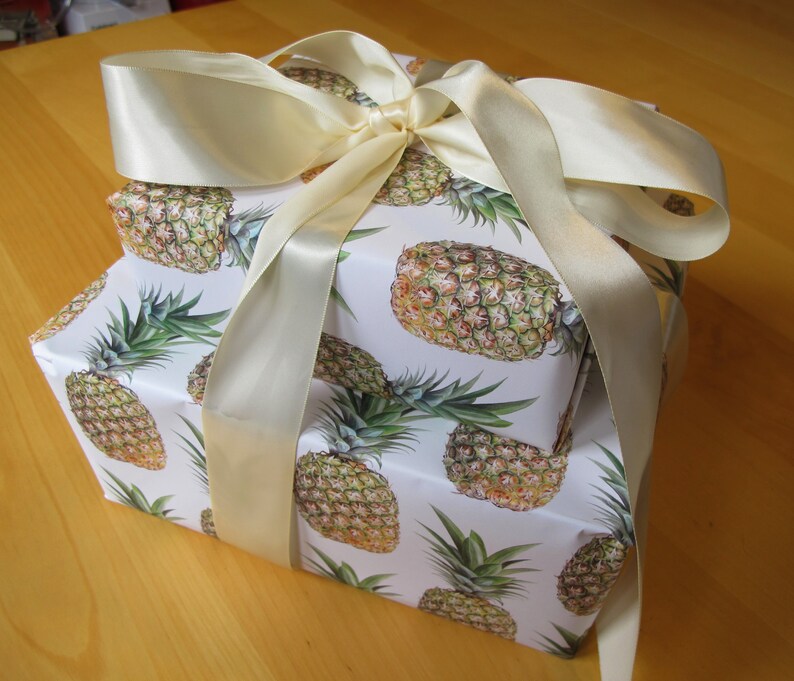 A stack of pineapple paper-wrapped gifts tied up with a luxurious cream silk ribbon.